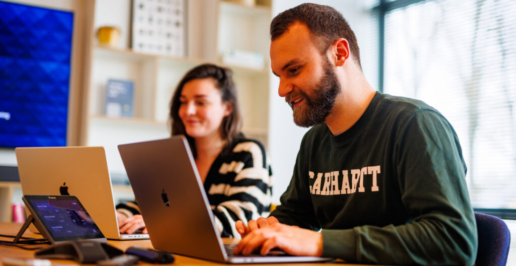 A male and female employee of Nixon Digital working on their computers in an office with smiling expressions.